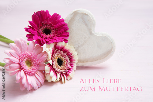 pink flowers and a white painted wooden heart on a pastel colored background,  german text Alles Liebe zum Muttertag, meaning All Love for Mother's Day
