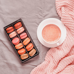 Bed with pink knitted plaid, coffee and macaroons.