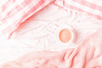 Bed with pink knitted plaid, coffee and macaroons.