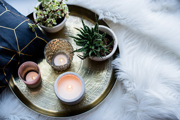 Cozy real home decoration, burning candles on golden tray with pillow on white faux fur on...