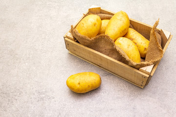 Raw unpeeled young potatoes in a wooden crate. New harvest, on sackcloth, stone background, copy space.