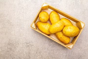 Raw unpeeled young potatoes in a wooden crate. New harvest, on stone background, copy space, top view