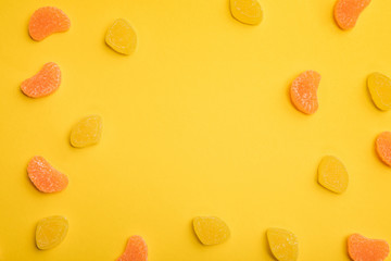 top view of delicious orange and lemon jellies scattered on yellow background