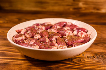 Ceramic plate with raw chicken hearts on wooden table