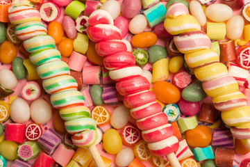 Fototapeta na wymiar top view of bright delicious multicolored caramel candies and swirl lollipops on wooden sticks