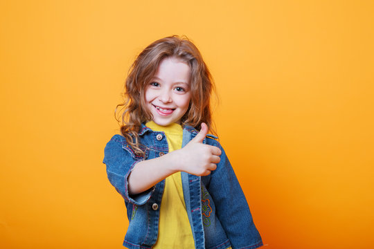 Cute little girl showing thumbs up on orange background