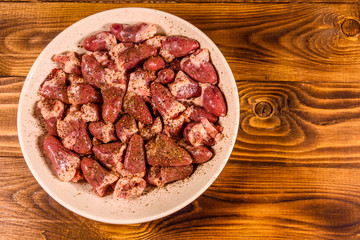 Ceramic plate with raw chicken hearts on wooden table. Top view