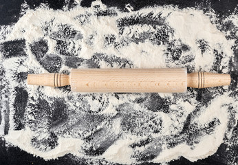 wooden rolling pin and white wheat flour scattered on a black background