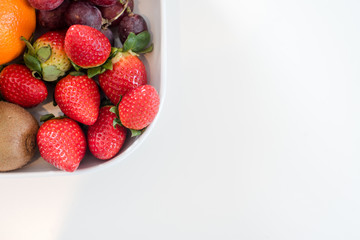 Fresh mixed sweet fruit on plate over white