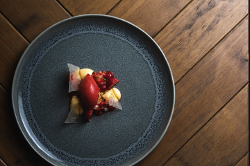 A top down shot on a wooden dark oat coffee table of a modern dessert made of Strawberry, White chocolate,Tarragon and Sichuan Pepper. Dish Designed and created by the Chef, unique dish.