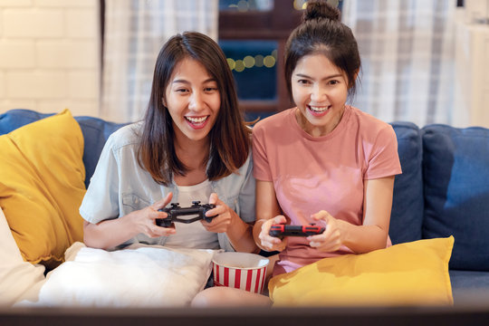 Candid Of Young Attractive Asian Homosexual Couple Of Lesbian Woman Sitting On Couch In Living Room At Home Enjoy And Excited Holding Console Playing Game Together. LGBT Family Pride In Asian Concept.