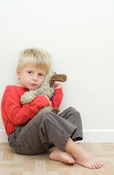 Lonely upset child sitting on the floor with his teddy bear.