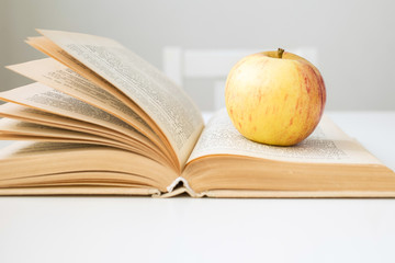 On the table is a book with an apple. A red-yellow apple is in front of a book. On the desk is an apple.