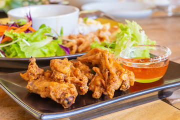 Thai style deep fried chicken wings with sauce and salad serve on a black plate.