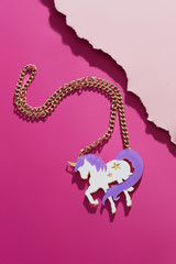 Shot of a stylish massive necklace with a pendant in the view of a unicorn. The accessory is isolated against the pink background, near pale pink ragged platform. Fashionable women's fashion item.
