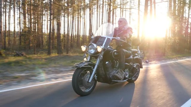 adult biker without helmet rides a motorcycle along a forest road at sunset 