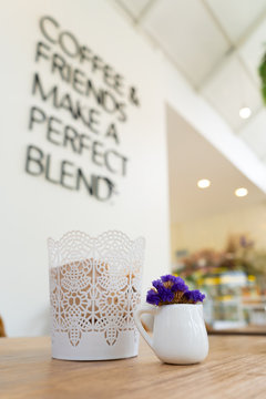 Small violet flower in a white cup with a sentence in the wall in a white vintage cafe