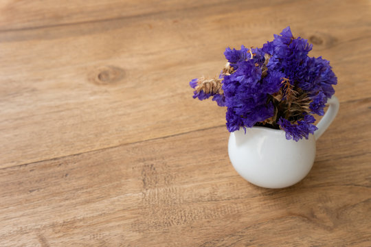 Small violet flower in a white cup on a wooden tablein vintage background