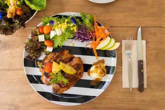 Chicken steak serve with mashed potato and salad on a black and white plate with a fork and a knife on a wooden table