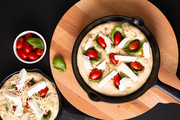 Food concept rising dough for Homemade organic Focaccia in skillet iron pan on black background with copy space