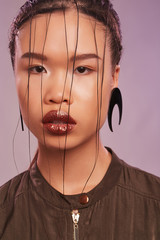Portrait of Korean lady with wet hair locks on her face, wearing massive earring in view of black...