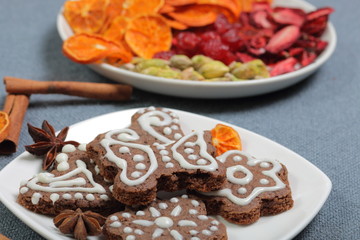 Gingerbread cookies decorated with a pattern of white glaze. On a background of gray fabric. Decorated with decorative elements of dried fruit, cinnamon sticks and anise stars.
