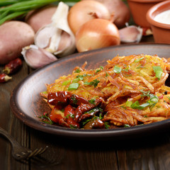 Homemade tasty potato pancakes in clay dish with sun-dried tomatoes and sour cream