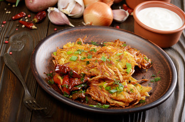 Homemade tasty potato pancakes in clay dish with sun-dried tomatoes and sour cream