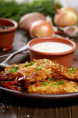 Homemade tasty potato pancakes in clay dish with sun-dried tomatoes and sour cream