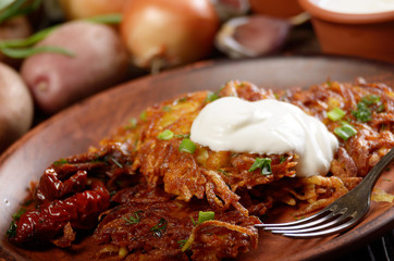 Closeup view at Homemade tasty potato pancakes in clay dish with sun-dried tomatoes and sour creram