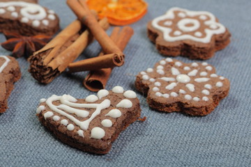 Gingerbread cookies decorated with a pattern of white glaze. On a background of gray fabric. Decorated with decorative elements of dried fruit, cinnamon sticks and anise stars.