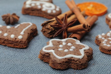 Fototapeta na wymiar Gingerbread cookies decorated with a pattern of white glaze. On a background of gray fabric. Decorated with decorative elements of dried fruit, cinnamon sticks and anise stars.