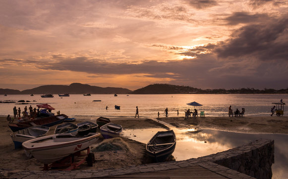 High contrast boats and tourists and locals at a bay surrounded by warm sea water at golden hour, at a beautiful summer sunset at Buzios, Brazil, next to Geriba beach