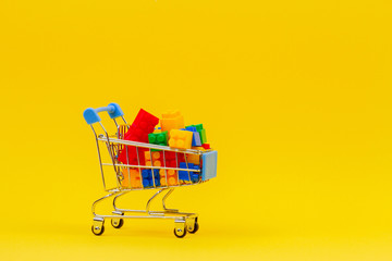 Shopping trolley cart full of colorful bricks on yellow background