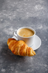 Cup of coffee and freshly baked croissants on gray background. Copy space.