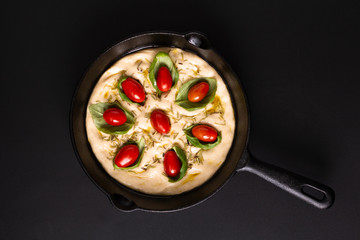 Food concept rising dough for Homemade organic Focaccia in skillet iron pan on black background with copy space