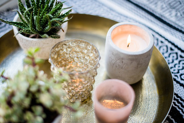 Real apartment interior decor, aromatic candles and plants on vintage tray with pillows and blanket on white windowsill