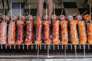 Charcoal grilled fermented sausage skewers named Sai krok Isaan. Local authentic Thai street food cooking for sale in the Bang Nam Pheung floating market. Bang Kachao, Thailand.