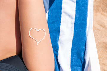 Sunscreen in the form of heart on woman's leg sunbathing on the towel by the sea