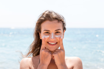 Beautiful young woman is posing at the camera with suncream on her face over the sea background