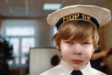 Sad offended little blond boy in a sailor cap with the inscription Sailor in Russian