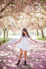 A young beautiful Asian woman in a white dress walks in a flowered park. Sakura. Blooming trees.