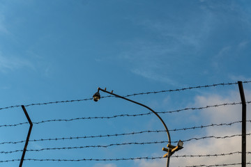 Two birds are perched on a cctv which is bordered by barbed wire against a background of bright...