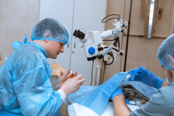 A professional ophthalmologist performs eye surgery with a microscope. The anesthesiologist...