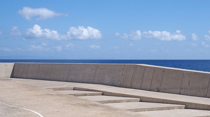 long image of a concrete sea wall with steps against a calm blue sea and sunlit blue sky