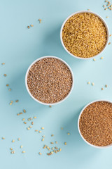 Uncooked crushed spelt, wheat and bulgur in a white bowl on pastel blue background. Top view, copy space, minimal idea 