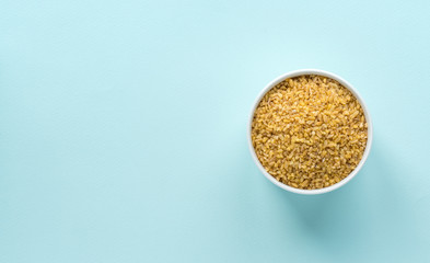 Uncooked bulgur in a white bowl on pastel blue background. Top view, copy space, minimal idea