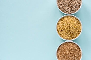 Uncooked crushed spelt, wheat and bulgur in a white bowl on pastel blue background. Top view, copy space, minimal idea
