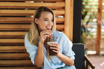Smiling young woman drinking juice while sitting at the cafe