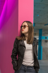 Fashioned girl in leather jacket in dark glasses in pink and blue  neon lights background. 